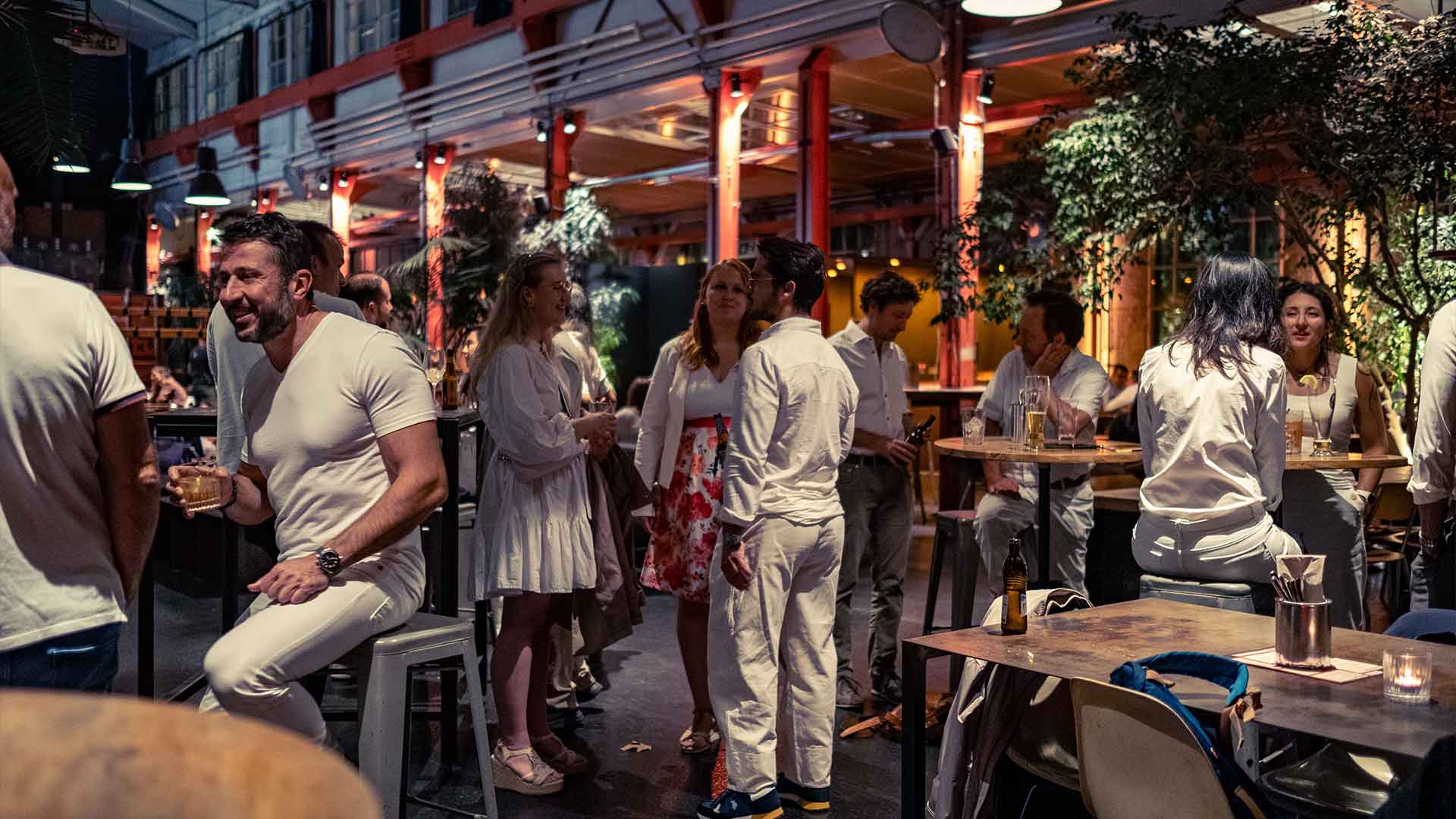 Patrons socializing in an outdoor evening setting at a lively bar with industrial decor.